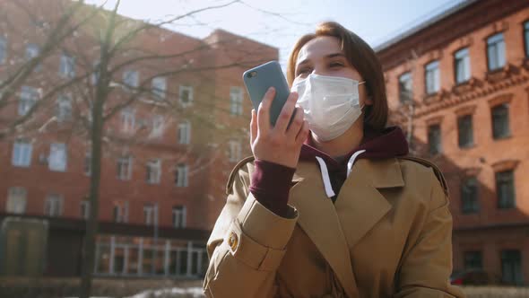 Tourist in protective medical mask walking in the street using phone, recording voice messages.