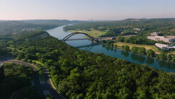 Aerial sweep of the iconic Pennybacker 360 bridge in Austin, Texas during hazy summer sunrise mornin