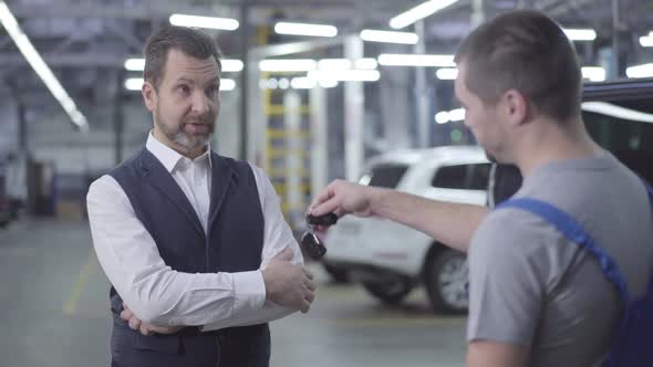 Portrait of Adult Bearded Caucasian Man in Elegant Outfit Taking Car Keys From Auto Mechanic