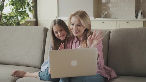 Happy Mother and Kid Daughter Waving Hands Looking at Web Camera Using Laptop for Video Call Smiling