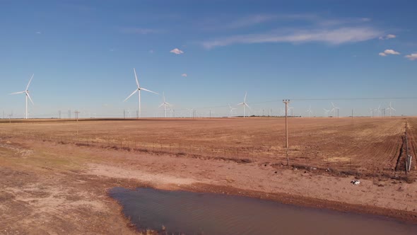 Drone shot of spinning wind turbines, electric poles in a dry area. Puddle of water is seen with win