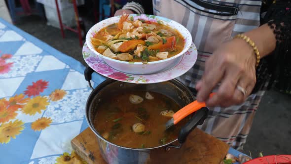 Thai woman pouring soup into bowl and putting it on a table.