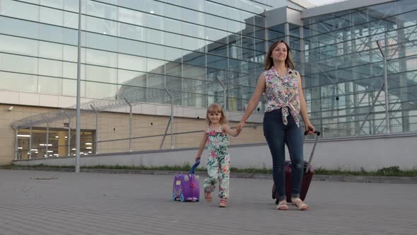 Mother and Daughter Walking From Airport. Woman and Child Carrying Suitcase Bags. Mom After Vacation