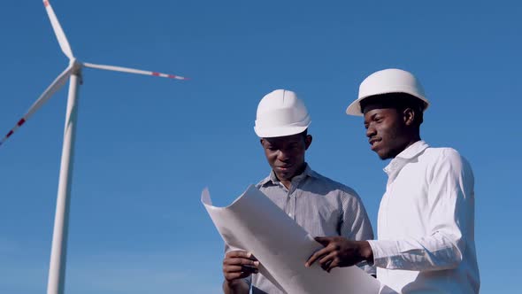 Two Male African American Electrical Engineers Stand Against the Backdrop of a Windmill at an Air