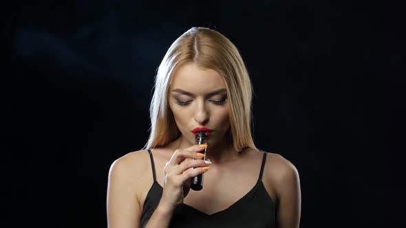 Blonde in a Spacious Room Smokes an Electronic Cigarette. Black Background