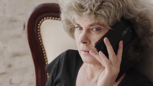 Older Woman Sitting on Chair Speaking on the Phone and Smiles at Camera