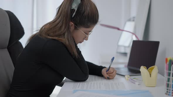 A Young Student of Colombian Universitary Sitting at a Table and Writing in Her Paper