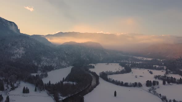 Drone shot of a mysterious landscape at sunset in the mountains covered with clouds in wintertime