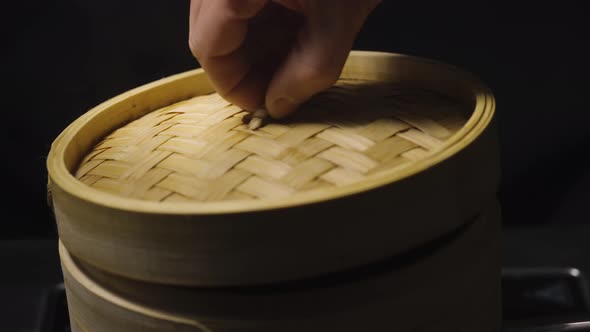 A Man's Hand Opens Lid of Bamboo Steamer Box Showing Chinese Dumplings Wonton Close Up on Black