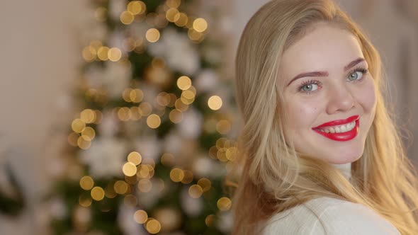 Portrait of Smiling, Blond, Girl with Long Hair in a Cozy Sweater on the Christmas Tree Background