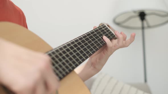 Portrait of a Handsome Boy Sitting on the Couch and Playing the Guitar