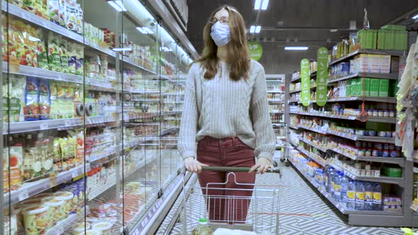 Closeup of a Young Woman's Hands Moving a Grocery Cart Through the Aisles of a Supermarket the