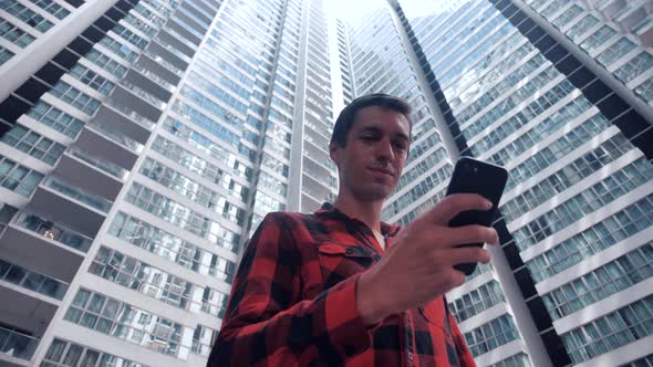Portrait of Young Man in Plaid Shirt Browsing His Smartphone in City