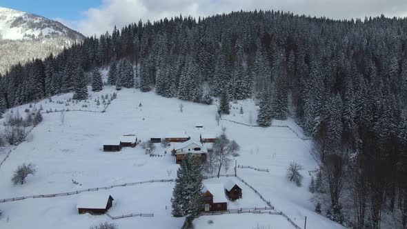 Aerial winter landscape with small rural houses between snow covered forest in cold mountains. alt