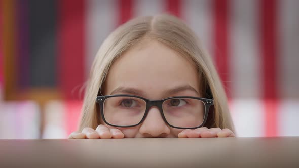 Closeup Eyes of Cheerful Teenage Girl in Eyeglasses Looking Around Hiding at Desk in Classroom