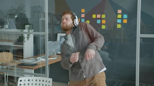 Slow Motion of Joyful Guy Dancing in Workplace Wearing Wireless Headphones