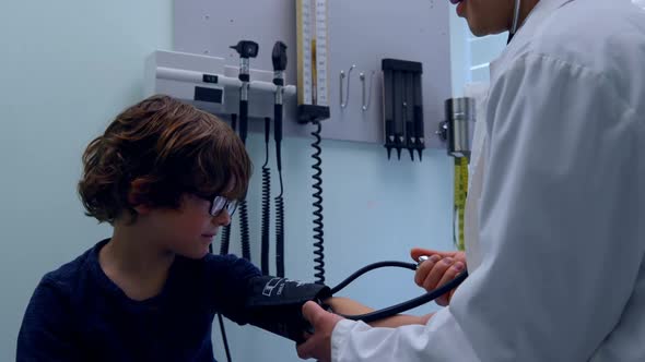 Side view of young asian male doctor checking blood pressure of caucasian boy patient in clinic 4k