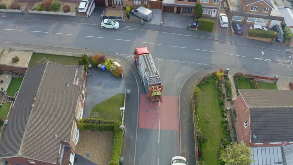 A bin lorry, refuse collection vehicle makes it way up the road as men load recycling bins into the