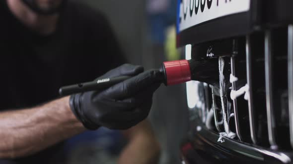 A Man in Black Gloves Brushes the Front Grille of the Car