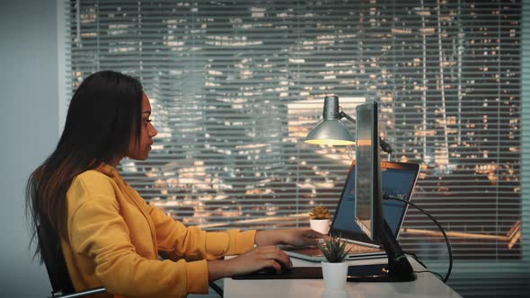 Side View of Black Female Videographer Working with Footage and Sound on Computer with Two Displays