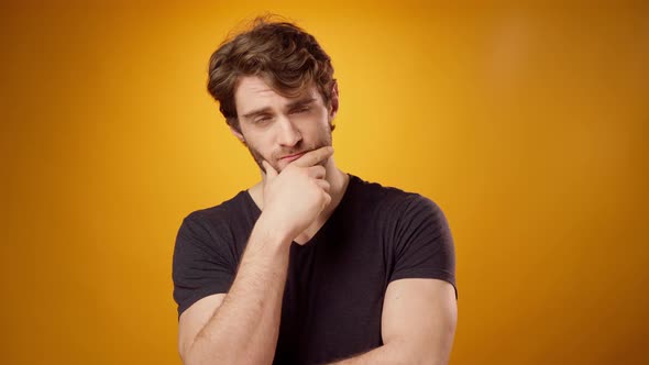 Thoughtful Young Man Pondering Something Touching His Chin Yellow Background