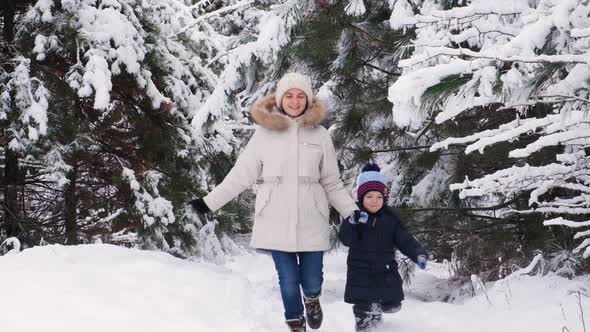 Mom and Son are Running in a Snowy Winter Forest Happy Parenthood and Family Vacation Slow Motion