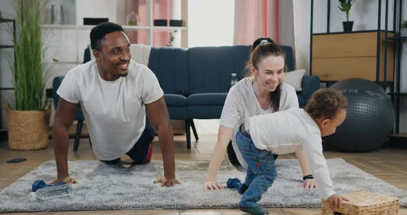 Couple Doing Sport Exercises with Push-Ups from the Floor Near their Playful Small Kid