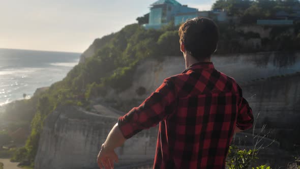 Young Man Traveler Raising His Hands High on Top of the Mountain Above Beautiful Landscape on Golden