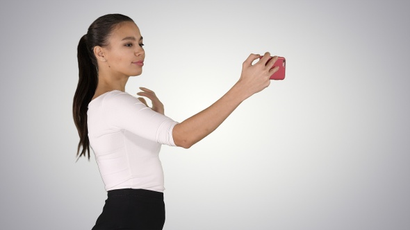 Pretty girl taking a selfie and walking on gradient background.