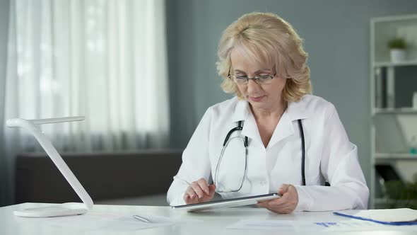 Female General Practitioner Reading Patient's Online Medical Records on Tablet