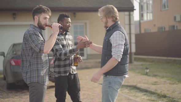 Two Caucasian and African American Men Standing in Front of Big House Drinking Beer