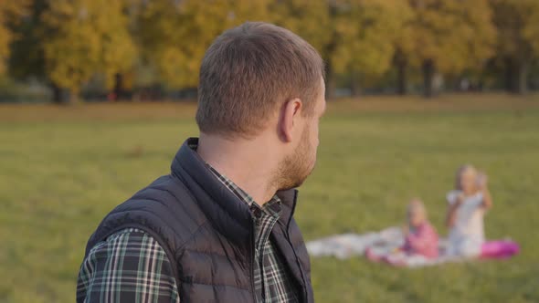 Exhausted Caucasian Man Waving To His Daughters on the Background and Touching His Face