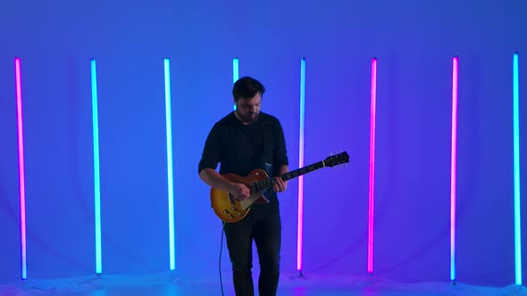 Musician Playing on Electric Guitar Against the Background of Multicolored Neon Lamps in the Studio