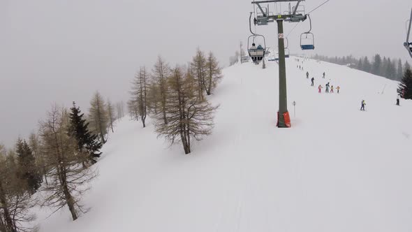 Going Up On A Chair Lift Under Snowfall In Mountains Above Ski Tracks