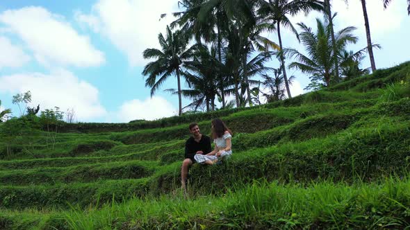 Young couple sitting on green terraces with rice planted on agricultural farm in Bali