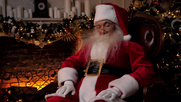 Santa Claus Falls Asleep Sitting on Chair on Background Fireplace Christmas Tree