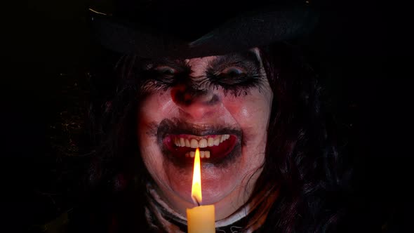 Sinister Woman with Scary Halloween Witch Makeup in Costume Making Voodoo Magic Rituals with Candle