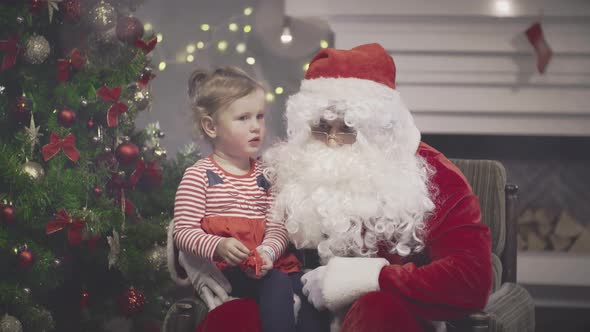 Santa Claus Talking to Cute Toddler Girl in Decorated Living Room