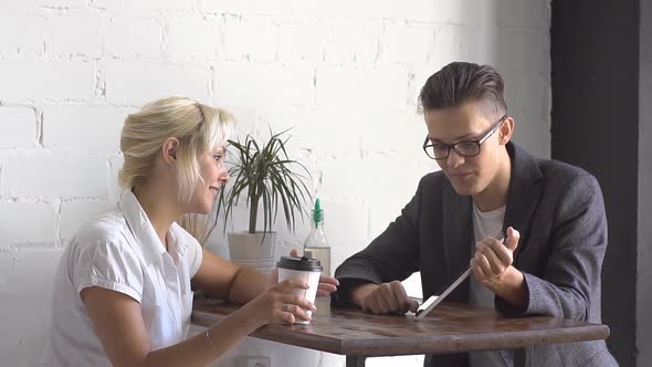 Man and Woman Sitting at the Table in Cafe. They Talking and Watching on Tablet