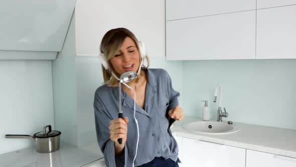 Positive blonde woman having fun, singing loudly in kitchen using ladle as microphone.