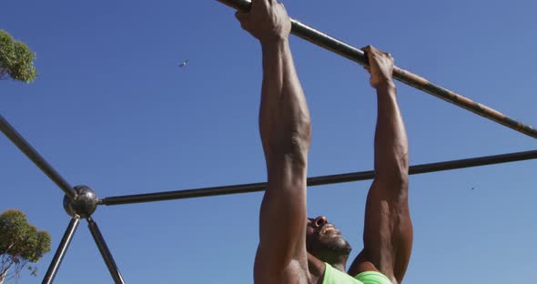 Fit african american man exercising outside, doing chin-ups on a climbing frame