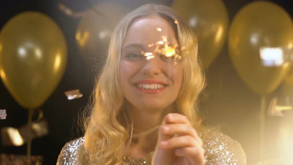 Smiling Blond Woman Waving Bengal Light Under Falling Confetti