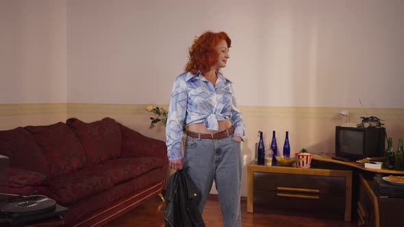 Zoom Out Happy Caucasian Redhead Woman Standing in Retro Bedroom Hanging Leather Jacket on Shoulder