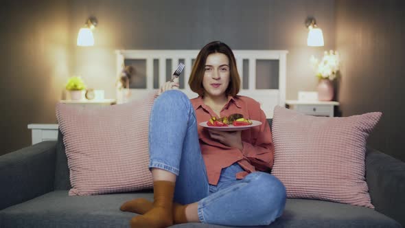 Young Woman Having a Dinner on the Couch in Front of the TV.