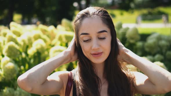 Charming Woman Straightens Her Hair in the Wind Closeup and Smiles at Camera.