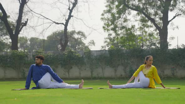 Half Spinal Twist Yoga pose or Ardha Matsyendrasana is being done by an Indian couple