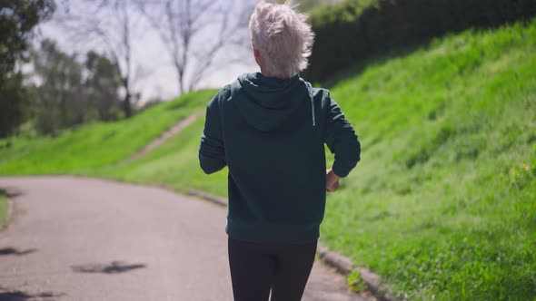 Live Camera Follows Fit Senior Sportswoman Jogging in Slow Motion in Sunlight