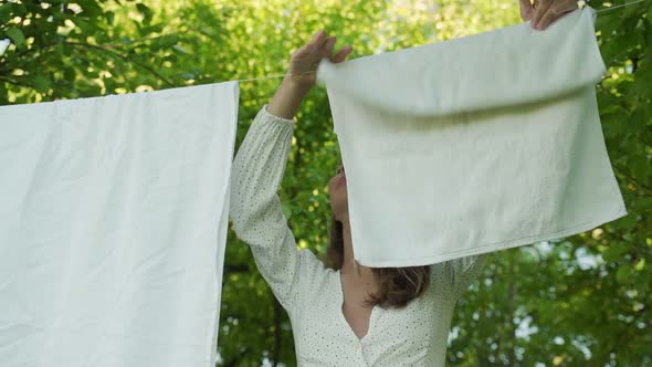 Young Woman Hangs Clean Underwear on a Clothesline in the Fresh Air Against the Background of Apple