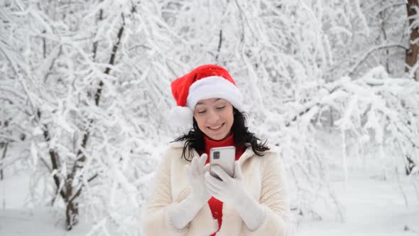 Beautiful Girl in Winter Clothes of Red and White Colors Smiles and Writes a Message on Her Phone