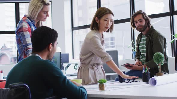 Diverse office colleagues wearing face masks discussing over blueprint plan at modern office